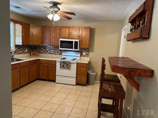 301 Gooseneck Ct, Forest, VA 24551 - kitchen with stainless steel microwave, white range with electric stovetop, backsplash, light countertops, and brown cabinets