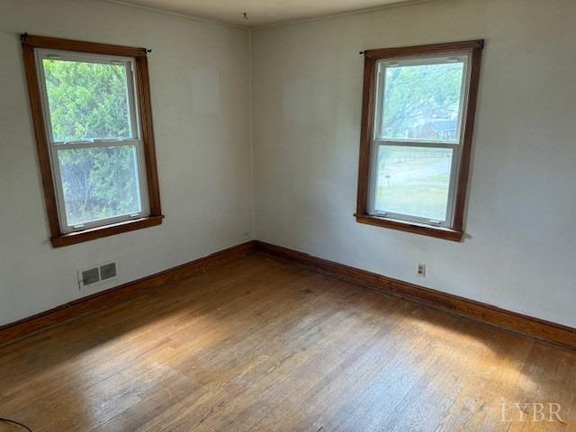 empty room featuring baseboards, plenty of natural light, wood finished floors, and visible vents