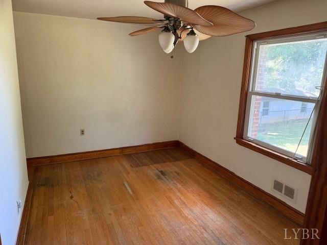 empty room with a healthy amount of sunlight, wood finished floors, and visible vents