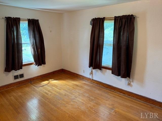 unfurnished room featuring baseboards, visible vents, and wood finished floors