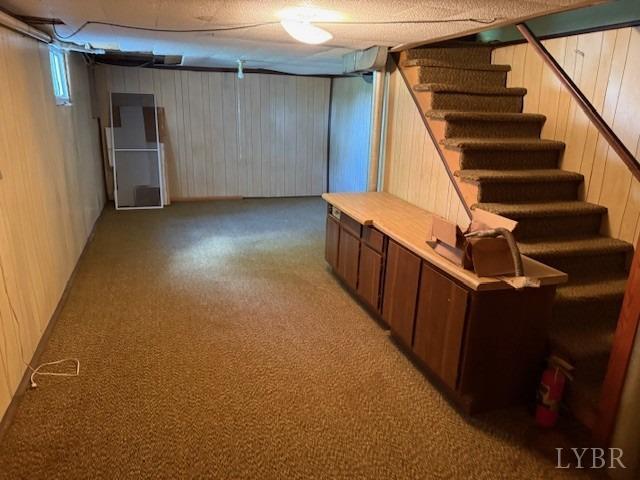 finished basement with light colored carpet, wooden walls, and stairway