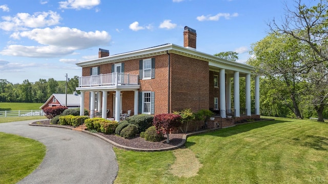 view of home's exterior featuring a chimney, brick siding, fence, a balcony, and a yard