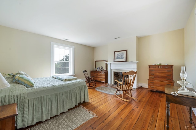 bedroom with a fireplace, baseboards, visible vents, and hardwood / wood-style floors