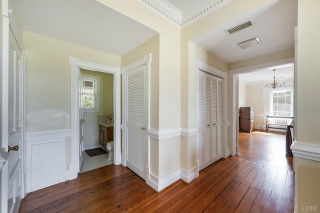 hallway with an inviting chandelier, baseboards, hardwood / wood-style flooring, and visible vents