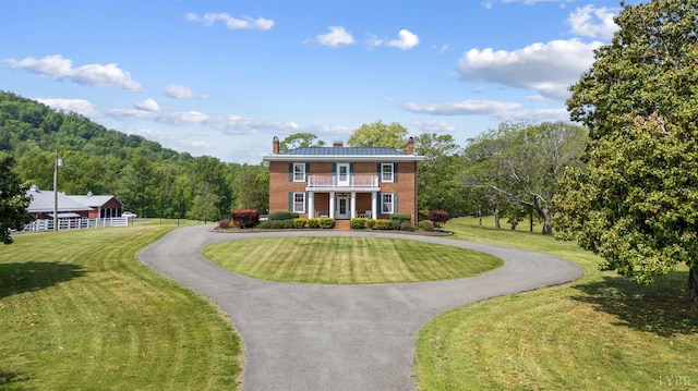 view of front of home featuring brick siding, curved driveway, a chimney, and a balcony
