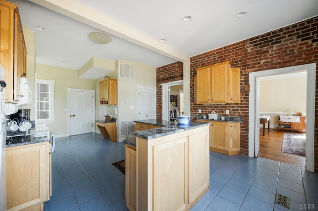 kitchen with light brown cabinets, white microwave, dark tile patterned floors, and brick wall