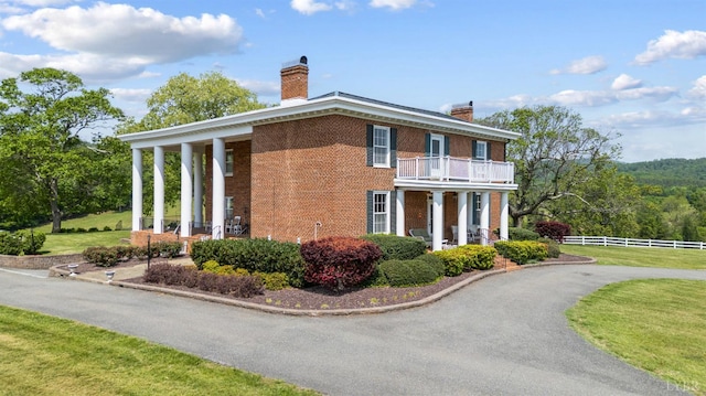 view of property exterior with fence, brick siding, a chimney, a balcony, and a yard