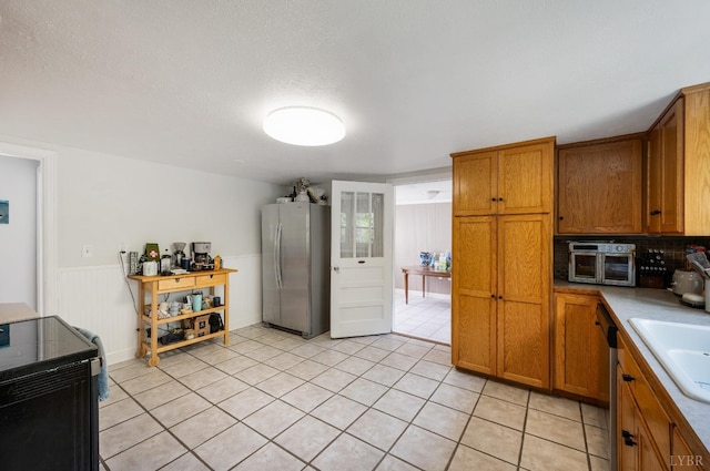 906 Elon Rd, Madison Heights, VA 24572 - kitchen with stainless steel appliances, brown cabinetry, light tile patterned floors, a sink, and wainscoting