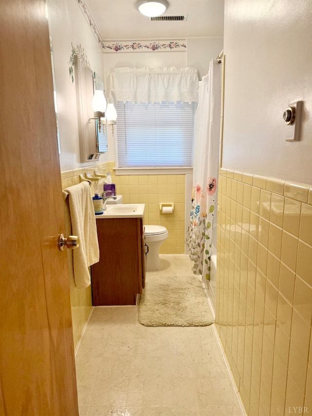 bathroom featuring tile walls, toilet, a wainscoted wall, vanity, and visible vents