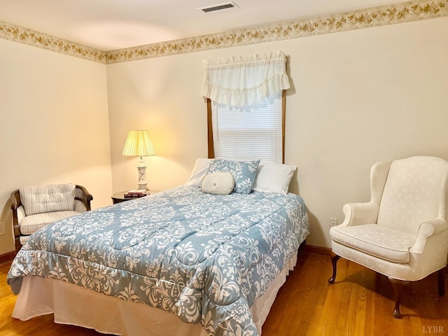 bedroom with baseboards, visible vents, and wood finished floors