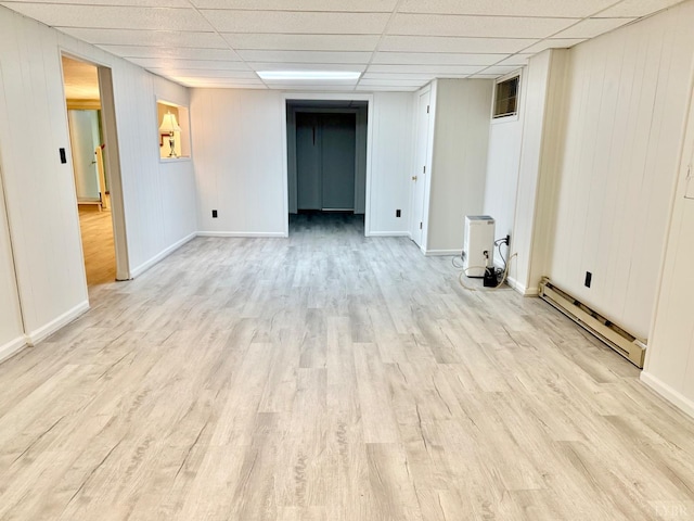 finished basement with a drop ceiling, light wood-style flooring, baseboards, and a baseboard heating unit