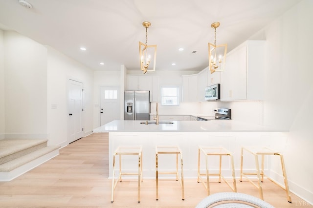 kitchen with a sink, white cabinetry, a kitchen breakfast bar, a peninsula, and appliances with stainless steel finishes