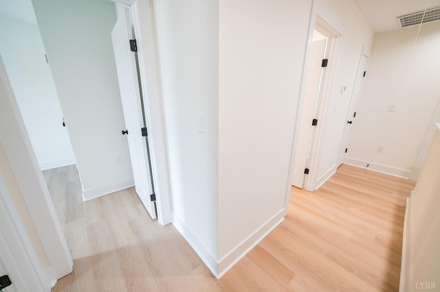 hallway with light wood-style flooring, baseboards, and visible vents