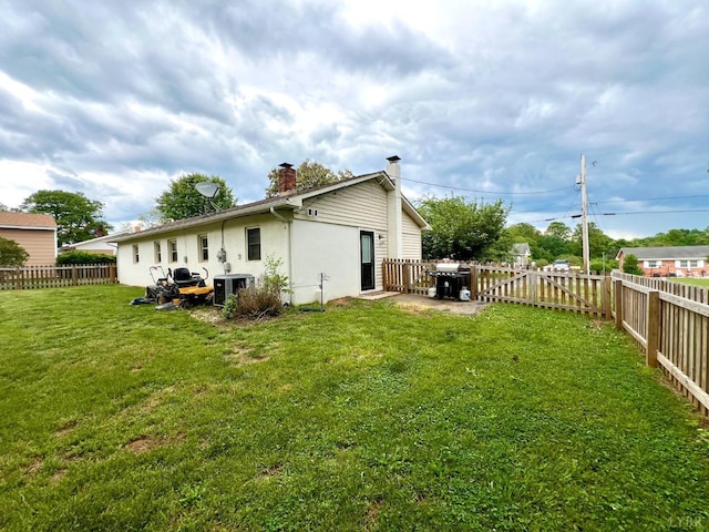 back of house featuring cooling unit, a chimney, a lawn, and a fenced backyard