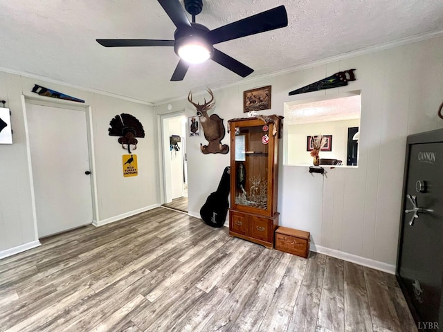 interior space featuring wood finished floors, crown molding, a textured ceiling, baseboards, and ceiling fan