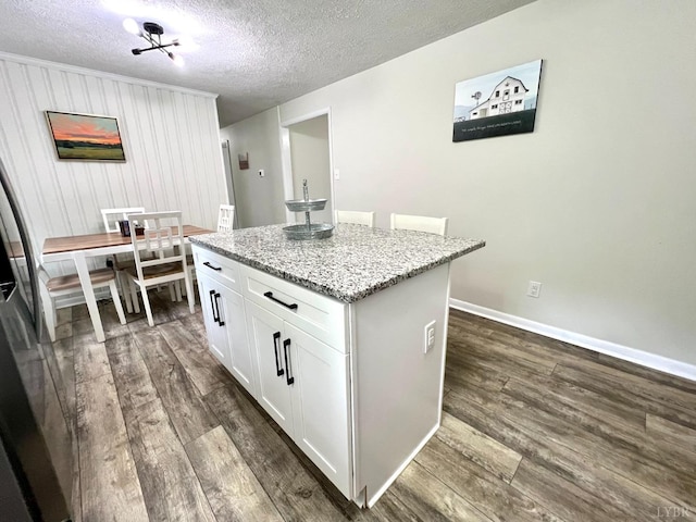 kitchen featuring a textured ceiling, dark wood-style flooring, white cabinets, light stone countertops, and a kitchen island