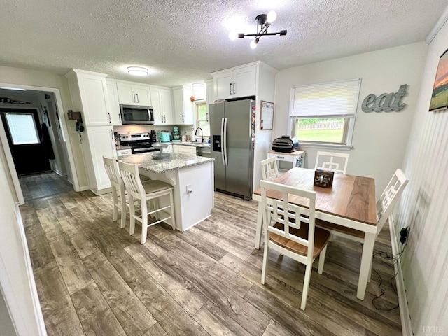 kitchen with a sink, stainless steel appliances, wood finished floors, white cabinetry, and a kitchen island