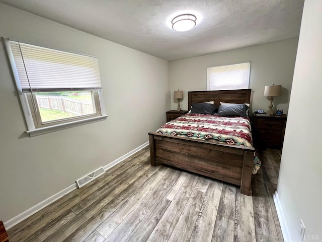 bedroom featuring wood finished floors, visible vents, and multiple windows