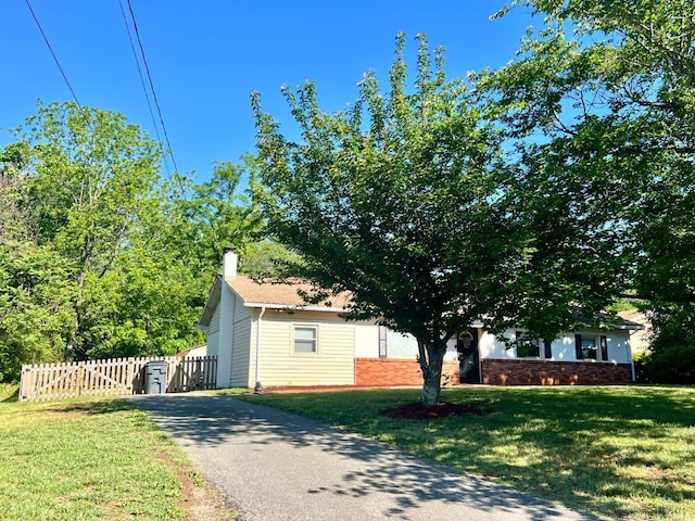 view of home's exterior with fence, brick siding, driveway, a chimney, and a lawn