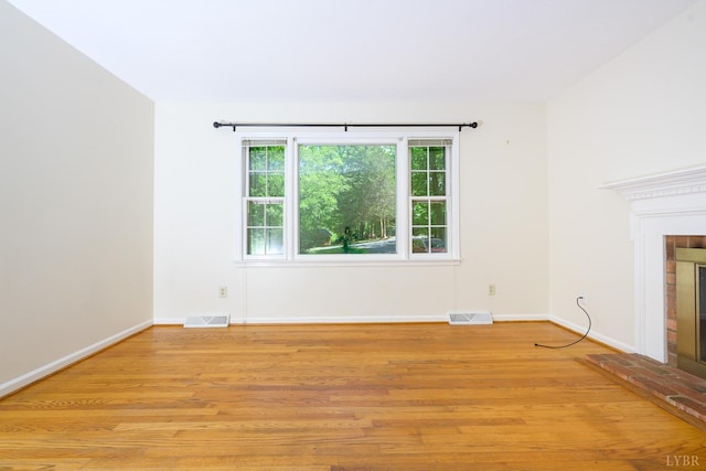 unfurnished living room with baseboards, light wood finished floors, a fireplace, and visible vents
