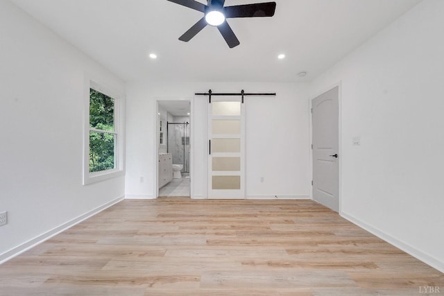 unfurnished bedroom featuring a barn door, light wood-type flooring, recessed lighting, ensuite bathroom, and baseboards