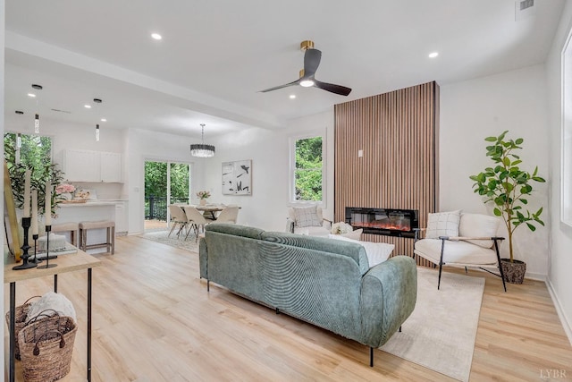 living room featuring light wood-style flooring, ceiling fan, a glass covered fireplace, recessed lighting, and baseboards