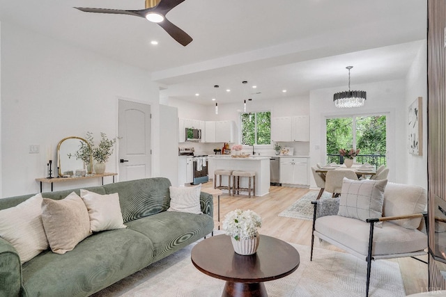 living area with light wood-style floors, recessed lighting, ceiling fan, and a chandelier
