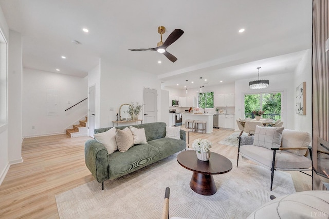 living area featuring light wood-type flooring, stairway, a ceiling fan, recessed lighting, and a chandelier