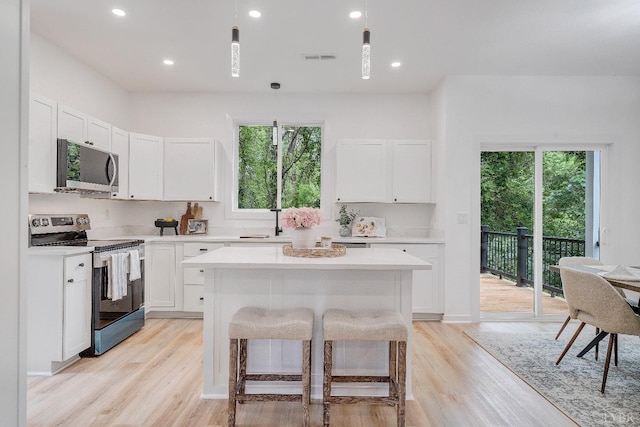 kitchen with appliances with stainless steel finishes, light countertops, light wood finished floors, a kitchen island, and recessed lighting