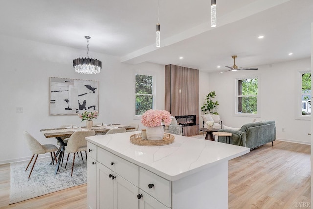 kitchen with light wood-type flooring, white cabinetry, a kitchen island, pendant lighting, and baseboards