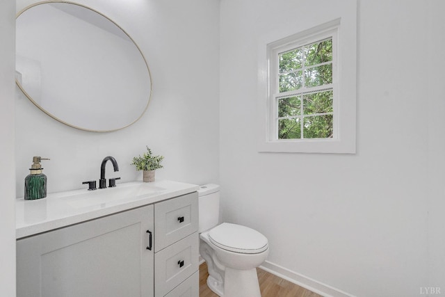 half bath with wood finished floors, toilet, vanity, and baseboards