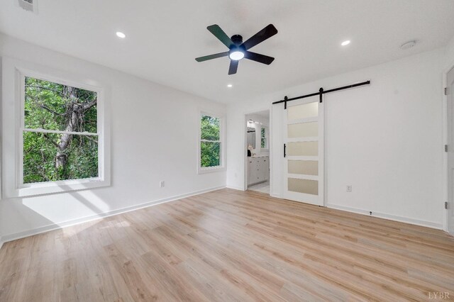empty room featuring a barn door, plenty of natural light, ceiling fan, light wood-style flooring, and recessed lighting