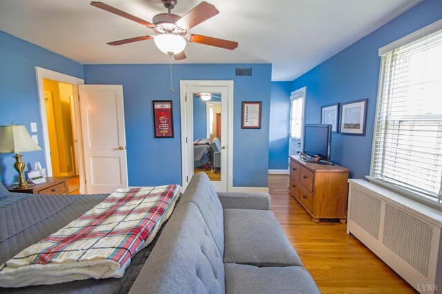 bedroom featuring radiator heating unit, light wood-style floors, multiple windows, and a ceiling fan