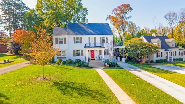 view of front of property with a balcony, concrete driveway, a front lawn, and a chimney