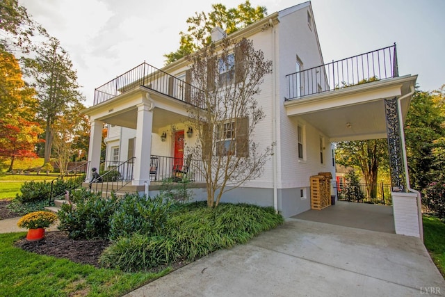 view of side of property featuring a balcony, a porch, driveway, a carport, and stucco siding