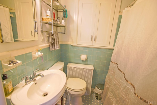 bathroom with a sink, toilet, wainscoting, tile walls, and a shower with curtain