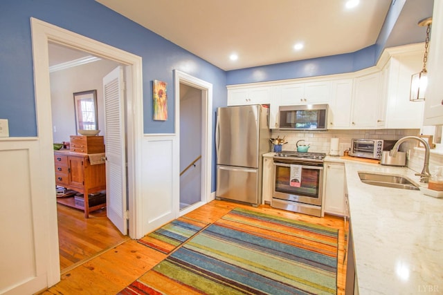 kitchen featuring appliances with stainless steel finishes, a sink, white cabinets, light stone counters, and a wainscoted wall