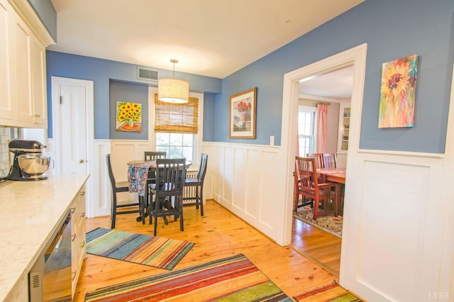 dining area with light wood-type flooring, healthy amount of natural light, a wainscoted wall, and a decorative wall