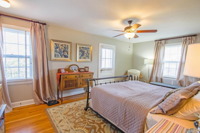 bedroom with multiple windows, light wood-type flooring, baseboards, and a ceiling fan