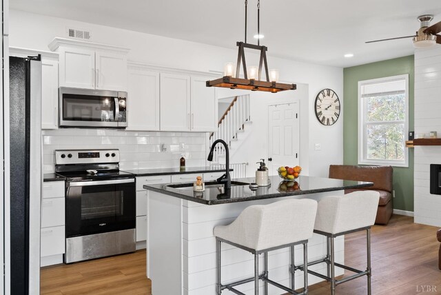 71 Patrick Ct, Madison Heights, VA 24572 - kitchen featuring appliances with stainless steel finishes, dark countertops, light wood-style flooring, white cabinets, and a breakfast bar area