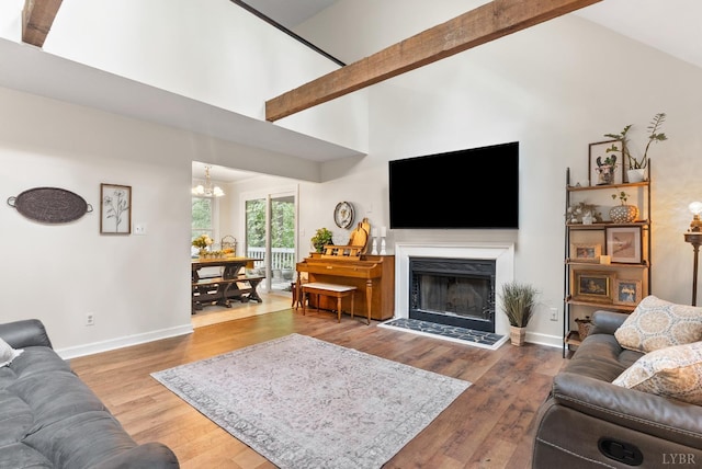 living room with a chandelier, wood finished floors, baseboards, high vaulted ceiling, and a fireplace with raised hearth