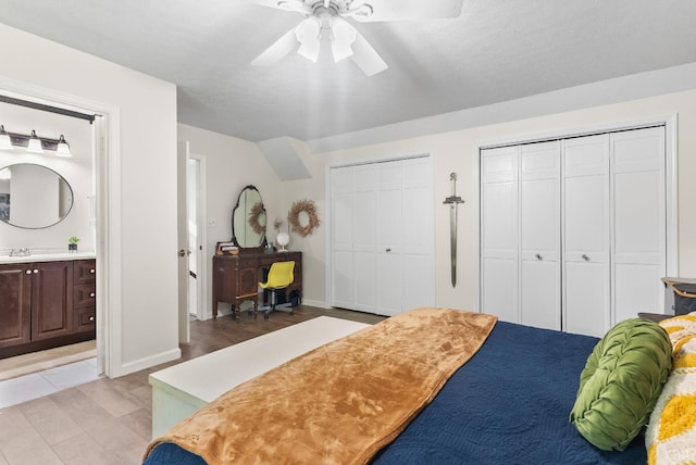 bedroom with multiple closets, a sink, connected bathroom, a ceiling fan, and baseboards