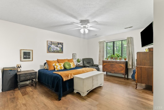 bedroom featuring light wood-style floors, a textured ceiling, and ceiling fan