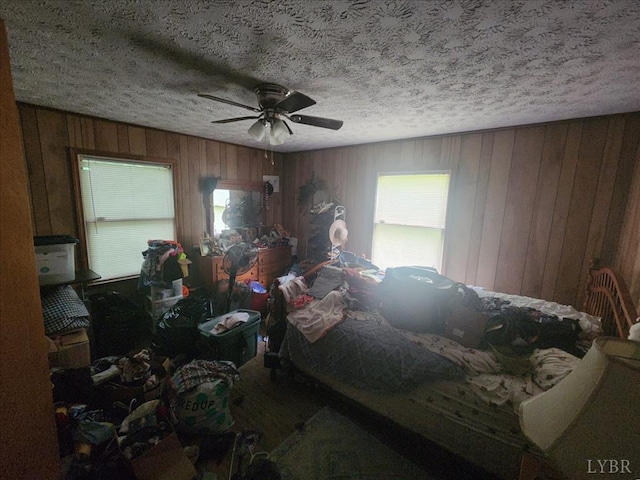 bedroom with wooden walls, a textured ceiling, and ceiling fan