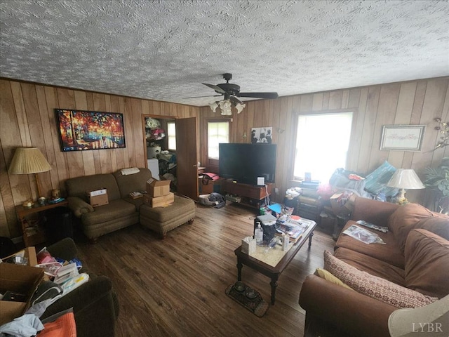 living area featuring wood finished floors, ceiling fan, wooden walls, and a textured ceiling