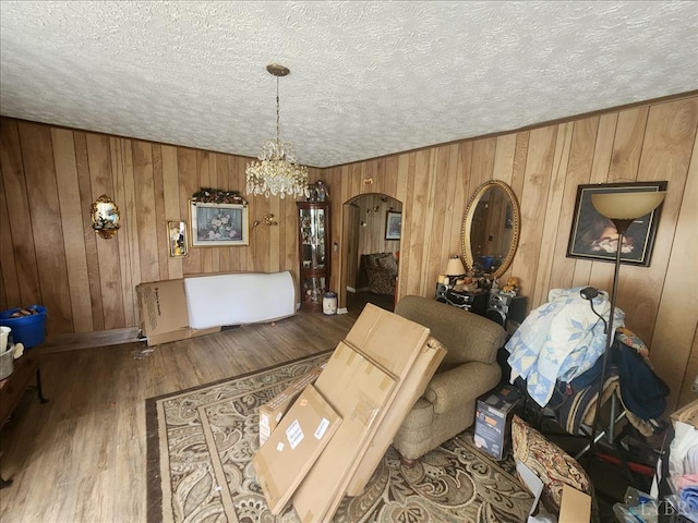 living area featuring arched walkways, a textured ceiling, a chandelier, wood walls, and wood finished floors