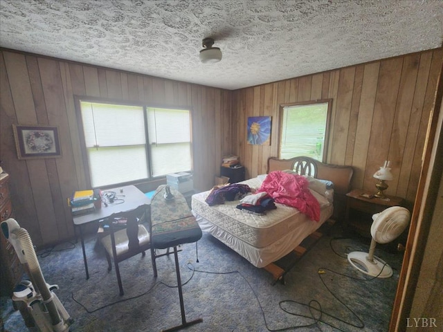 bedroom featuring wooden walls, multiple windows, a textured ceiling, and carpet