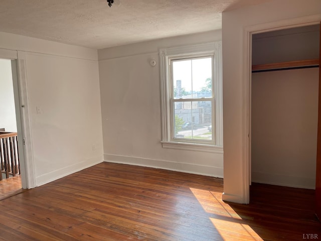unfurnished bedroom with multiple windows, hardwood / wood-style flooring, a textured ceiling, and baseboards