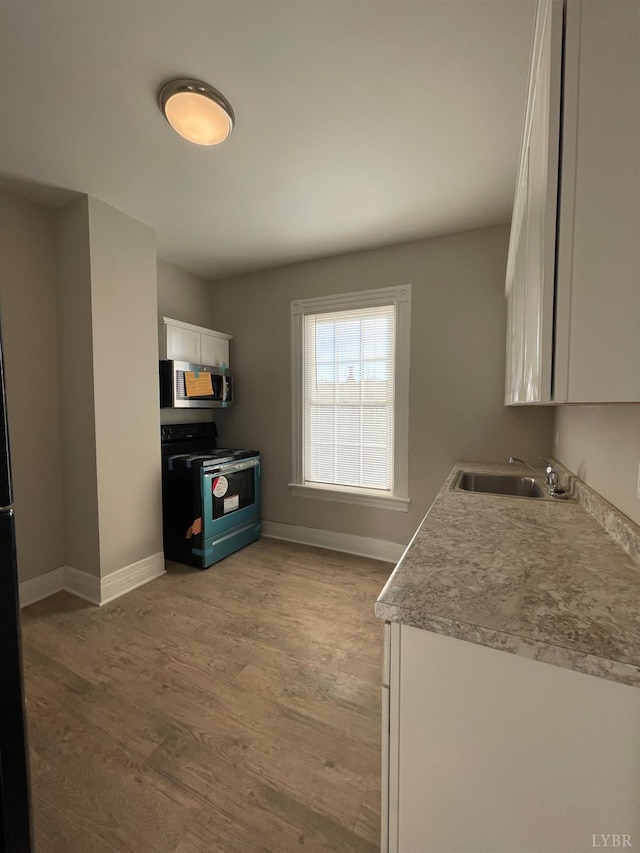 kitchen featuring black range with electric stovetop, stainless steel microwave, a sink, white cabinetry, and light wood-style flooring