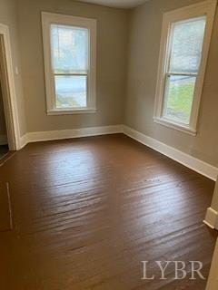spare room featuring baseboards and dark wood-type flooring